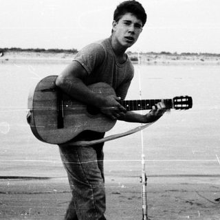 Young man holding acoustic guitar on beach.