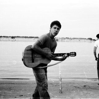 Young man holding acoustic guitar on beach.