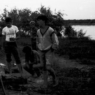 Group camping by water, cooking over fire.