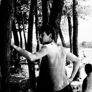 Shirtless man throwing frisbee near water.