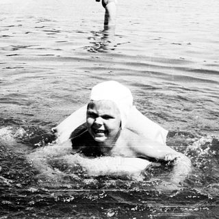 Person wrapped in white sheet swimming in crowded water.