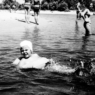 A woman swims in water with others on shore.