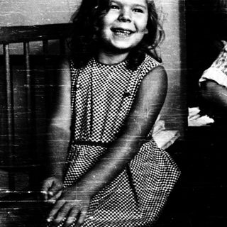Two children smiling indoors, one standing, one sitting.