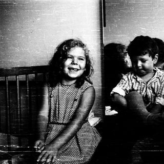 Two children smiling indoors, one standing, one sitting.
