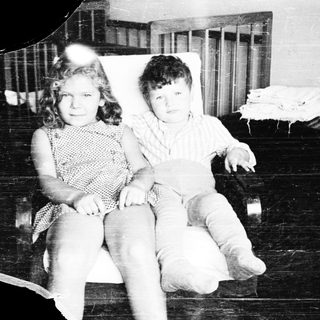 Two children sitting together indoors, mid-20th century.