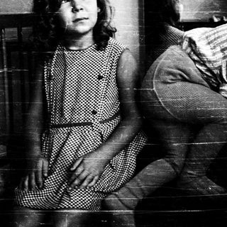 Two children sitting against a wall.