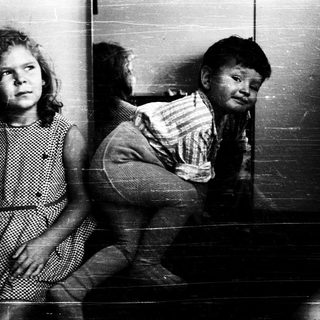 Two children sitting against a wall.