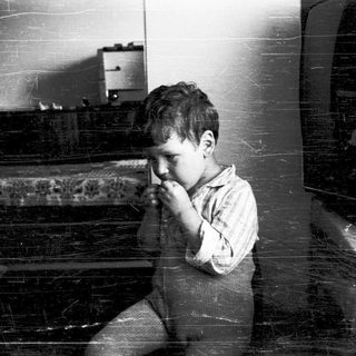 Young boy sitting indoors, covering mouth.