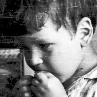 Young boy sitting indoors, covering mouth.