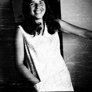 Smiling woman in vintage dress leaning against wall.