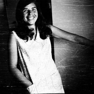 Smiling woman in vintage dress leaning against wall.