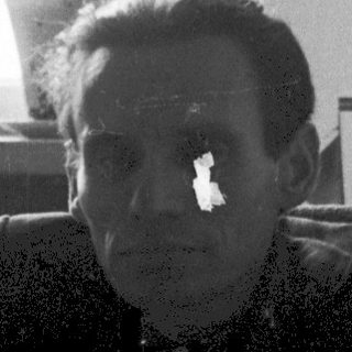 A man sitting indoors near a window, holding a glass.
