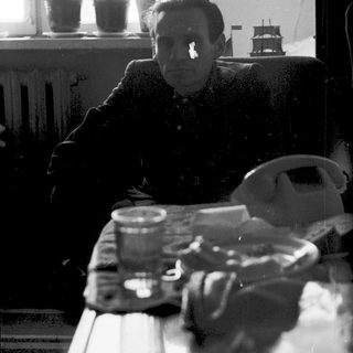 A man sitting indoors near a window, holding a glass.