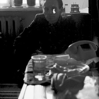 A man sitting indoors near a window, holding a glass.