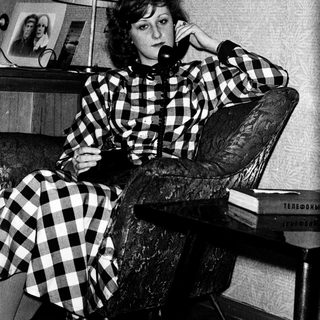 Woman in checkered dress talking on vintage phone.
