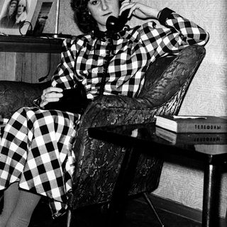 Woman in checkered shirt talking on vintage phone.