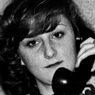 Woman in checkered shirt talking on vintage phone.