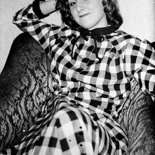 Young woman posing with cat in checkered shirt.