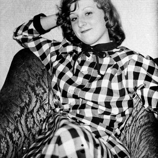 Young woman posing with cat in checkered shirt.