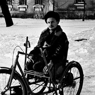 Child riding a tricycle in snowy outdoor setting.