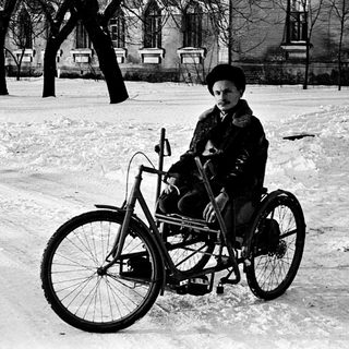 Child riding a tricycle in snowy outdoor setting.