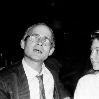 Two people, man in suit and woman in blouse, at an indoor event.