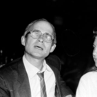 Two people, man in suit and woman in blouse, at an indoor event.