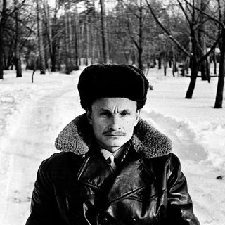 Man in winter attire standing outdoors in snowy forest.