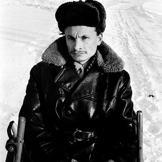 Man in winter attire pulling sled in snowy forest.