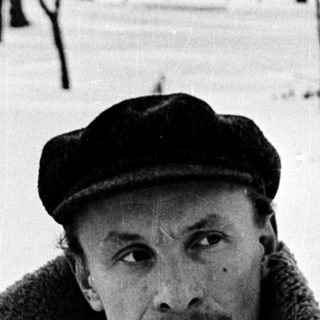 Man in winter attire sitting outdoors on snow.