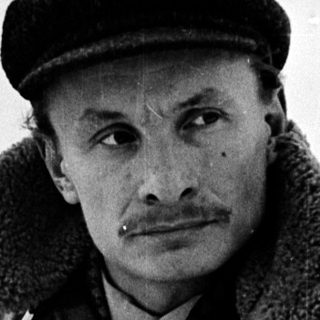 Man in winter attire sitting outdoors on snow.