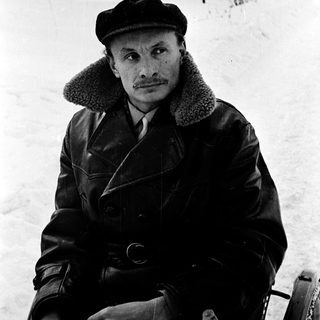 Man in winter attire sitting outdoors on snow.