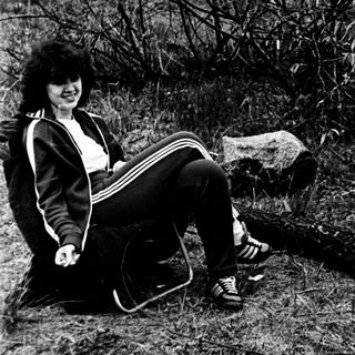 Person sitting outdoors near water, holding a camera.