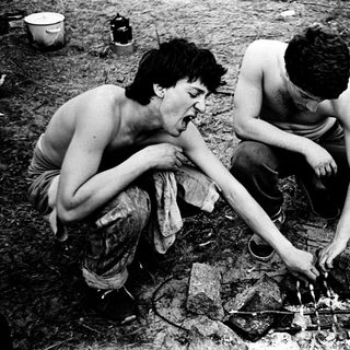 Two men cooking over an open fire outdoors.