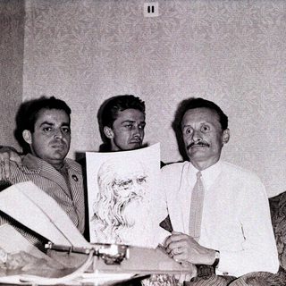 Three men examining a portrait sketch indoors.
