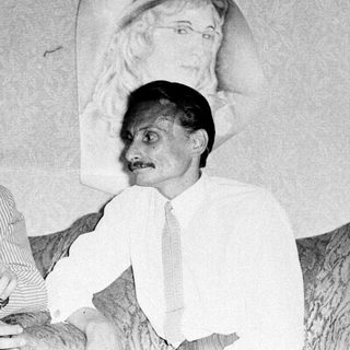 Two men posing together with a mural portrait in background.