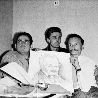 Three men examining a portrait drawing of a bearded man.