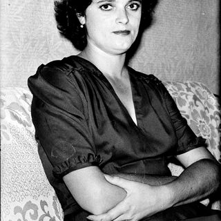 Woman in 1940s-style dress, seated with crossed arms.
