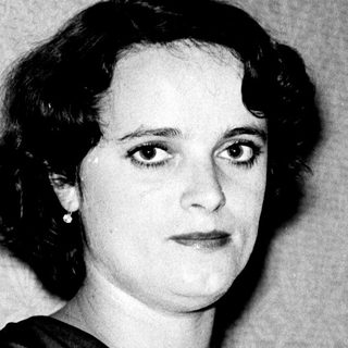 Woman in 1940s-style dress, seated with crossed arms.