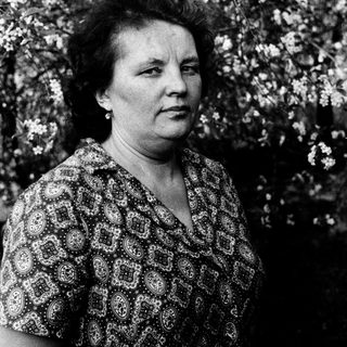 Woman in patterned blouse outdoors amid blossoming trees.