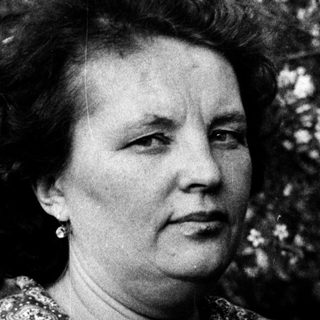 Woman in patterned blouse outdoors amid blossoming trees.
