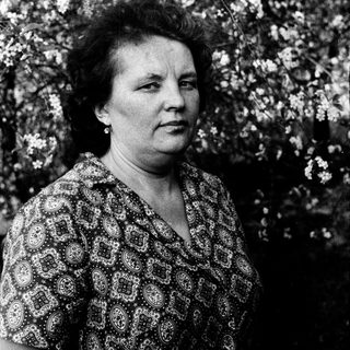 Woman in patterned blouse outdoors amid blossoming trees.