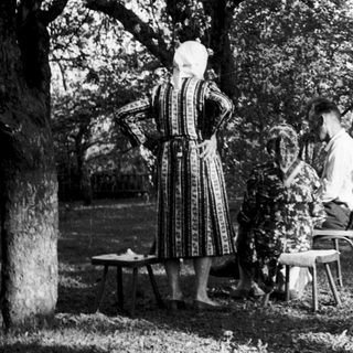 Vintage outdoor scene with women in traditional attire pouring liquid.