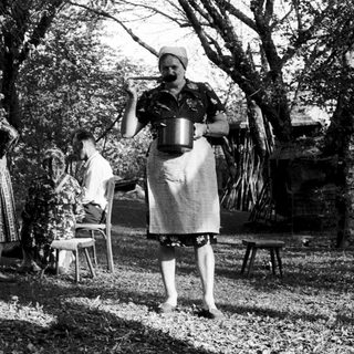 Vintage outdoor scene with women in traditional attire pouring liquid.