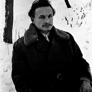 Man in winter coat sitting outdoors in snowy landscape.