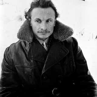 Man in winter coat posing outdoors in snowy landscape.