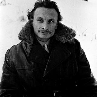 Man in winter coat posing outdoors in snowy landscape.