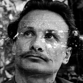 Man in outdoor setting, mid-20th century attire, thoughtful expression.