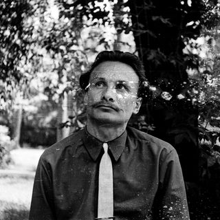 Man in outdoor setting, mid-20th century attire, thoughtful expression.