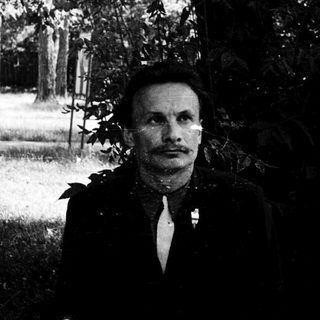 Man in formal attire posing outdoors among trees.